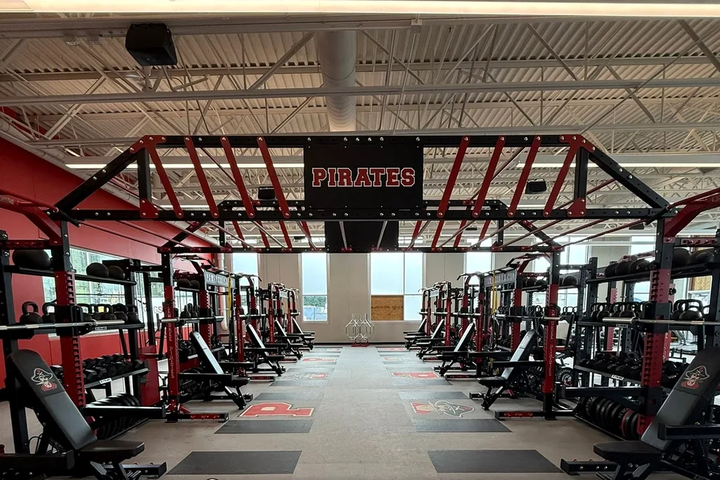 Pewaukee High School weight room with rows of power racks under a Pirates sign, installed by AFS